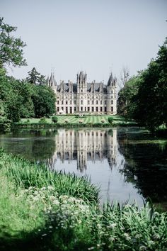 a large castle sitting on top of a lush green field next to a lake in front of it