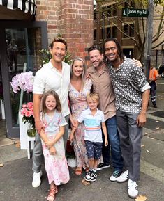 a group of people standing next to each other in front of a building with flowers