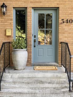 a blue front door with a planter on the steps and a welcome mat in front