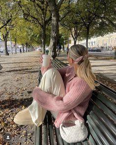 two women sitting on a park bench drinking coffee and looking at each other's hands