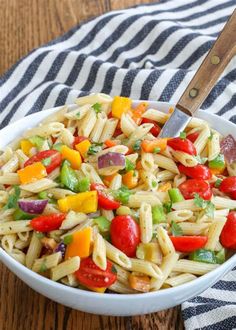 a white bowl filled with pasta salad on top of a wooden table next to a striped towel