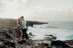 a man and woman standing on the rocks by the ocean with their arms around each other