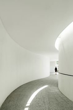 a person standing in the middle of a white room with curved walls and floor to ceiling windows