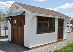 a white shed with brown shingles and windows