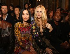 two women sitting next to each other in front of a group of people at a fashion show