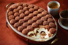 a cake in a pan next to a cup of coffee on a red table cloth