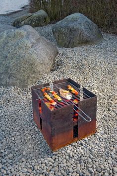 a grill that is sitting on some rocks by the water with food cooking on it