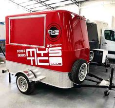 a red and silver food truck parked in a garage next to another white truck with the word food trucks on it's side