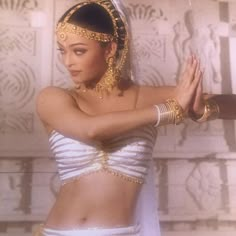 a woman dressed in white and gold with her hands on her hips, posing for the camera