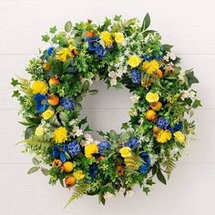 a wreath with yellow, blue and white flowers hanging on the side of a wall