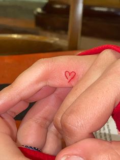 a person with a small heart tattoo on their ring finger and the other hand is holding something