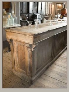 an old fashioned kitchen island with wine glasses on the top and below it, in front of