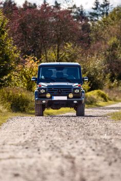 a black truck driving down a dirt road next to trees and bushes in the background