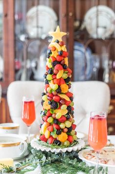 a christmas tree made out of fruit is on a table with wine glasses and plates