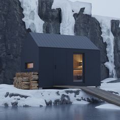 a small black cabin sitting on top of a snow covered mountain next to a body of water