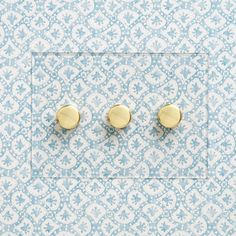 two pairs of gold - plated earrings on a blue and white patterned wallpaper