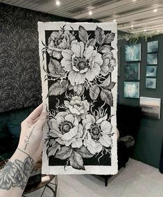 a person holding up a black and white drawing with flowers on it's side