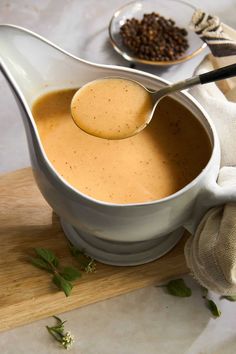 a gravy is being poured into a white gravy pot on a cutting board