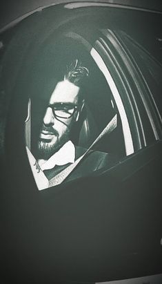 a man with glasses sitting in a car looking out the window and smiling at something