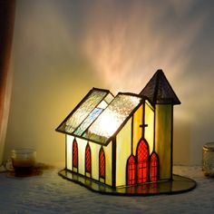 a small stained glass church lamp on a table next to a cup and candle holder