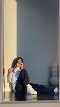 a woman sitting on the floor taking a selfie with her cell phone while wearing white sneakers