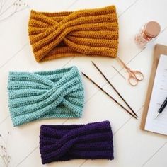 three knitted headbands on top of a table next to a clipboard