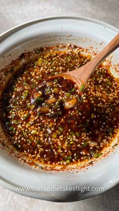 a wooden spoon in a white bowl filled with sesame seeds and seasoning on top