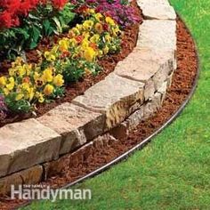 a garden with flowers and rocks in the grass next to a path that is lined with mulch