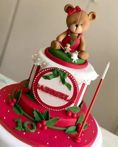 a red and white cake with a teddy bear sitting on it's top tier