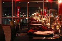 a long table is set with place settings and candles in front of large windows at night