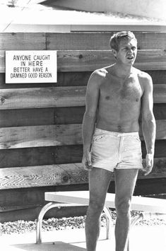 black and white photograph of a man standing in front of a wooden fence with no shirt on