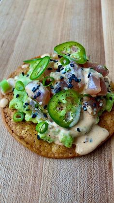 a cracker topped with cheese and vegetables on top of a wooden table next to a fork