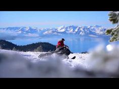 a man riding on the back of a snowboard down a snow covered slope next to a lake