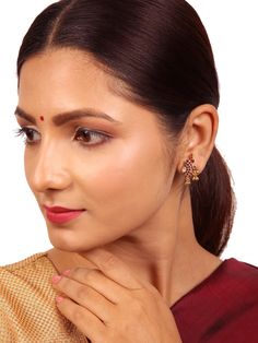 This classic antique Srinitha stud is crafted from 925 silver and elegantly accented with a touch of gold. The stud features a detailed elephant motif, and the timeless earrings are adorned with the captivating beauty of deep red spinal ruby gems and white zircon stones and ball dangles. This blend enhances the overall elegance of the earrings, making them a symbol of timeless grace and charm. Please refer to the pictures of the jewelry worn on a model to get a clear idea of the size. Condition: New. This product is intricately designed and meticulously handcrafted with exceptional care by our skilled silversmiths, employing traditional Indian techniques. Every jewelry piece from Sashastrends bears a 925-hallmark stamp!  Earring closure: Screw back. Material: 925 silver (gold polish), red Elegant Dual-tone Earrings, Elegant Latkans Earrings For Puja, Red Temple Jewelry Earrings, Ruby Chandbali Jhumkas, Elegant Meenakari Earrings For Puja, Elegant Intricate Design Earrings For Puja, Elegant Jhumkas For Puja, Touch Of Gold, Gold Polish