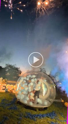 fireworks are lit up in the night sky behind a large bubble filled with balls and people