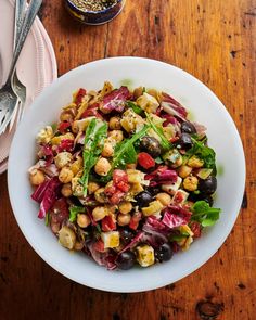 a white bowl filled with salad on top of a wooden table next to silverware