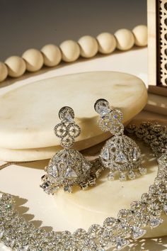 Elevate your allure with the Zeba - Classic AD Necklace Set adorned with Jhumka Earrings, a timeless piece crafted for sophistication. Available in two enchanting finishes, Rhodium (silver finish) or Gold plated, this set boasts intricate patterns of white AD stones, weaving triangular cut stones amidst circular designs created with smaller AD stones throughout. The accompanying lightweight Jhumka earrings, approximately 2 inches in length, exude elegance and boast a brilliant sparkle, adding a Heavy Silver Jhumkas For Reception, Silver Bridal Earrings With Stone Work For Reception, Silver Chandbalis With Intricate Design For Reception, Silver Jhumkas With Stone Work For Reception, Heavy Silver Chandbalis For Reception, Silver Chandbalis With Stone Work For Reception, Bollywood Style Silver Jhumkas For Reception, Elegant Sets With Intricate Design For Reception, Fusion Style Silver Bridal Earrings For Wedding