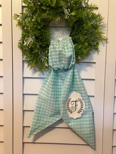 a green and white wreath hanging on the side of a house with a monogrammed bow