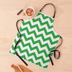 a green and white chevroned apron sitting on top of a wooden table next to utensils