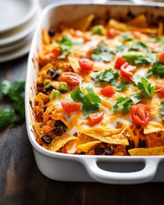 a white casserole dish filled with nachos and toppings on a wooden table