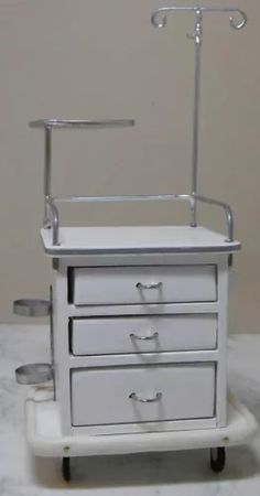 a white medical cart with three drawers on wheels and two handles, sitting on a marble surface