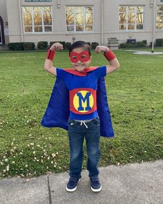 a young boy dressed as a super hero standing in front of a building with his hands on his head