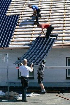 two men working on the roof of a house with metal shingles and blue tarps