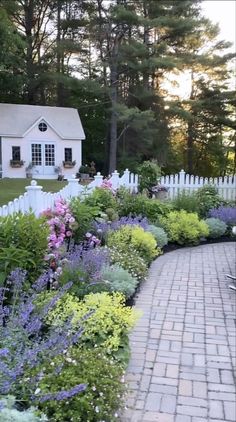 an outdoor garden with flowers, shrubs and a white house in the backround