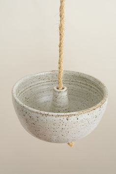 a white bowl hanging from a rope in the air with a light brown cord attached to it