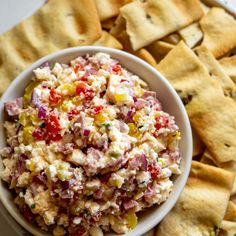 a white bowl filled with food next to crackers and chips on a table top