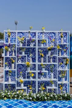 a blue and white display with flowers in vases on the wall next to a swimming pool