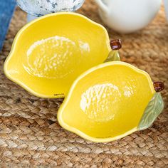 two yellow bowls sitting on top of a woven table cloth next to cups and vases