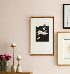 three framed pictures hang on the wall above a table with vases and flowers in front of it