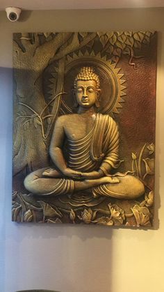 a buddha statue sitting on top of a wooden bench in front of a wall hanging